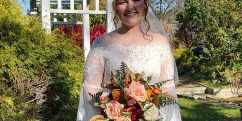 Bride smiling outdoors with a floral bouquet.