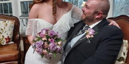Bride and groom smiling, holding bouquet indoors.