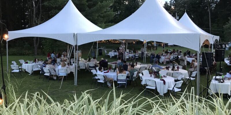 Outdoor event under white tents, people seated.